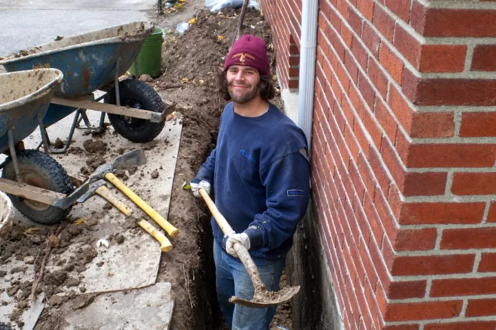 Clark crew member hand-digging a trench along a brick home's foundation