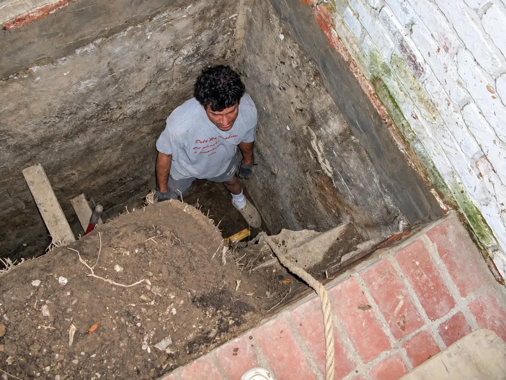 Crew member standing in a hand-dug excavation down to the footing