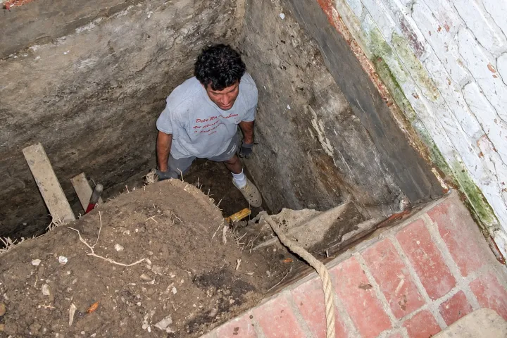 Crew member standing in a hand-dug excavation down to the footing