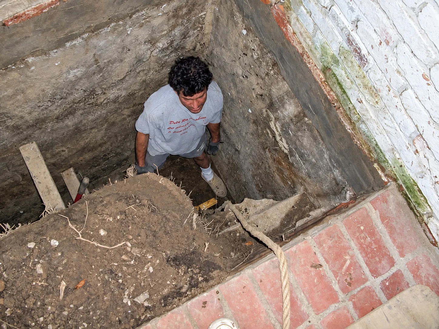 Crew member standing in a hand-dug excavation down to the footing