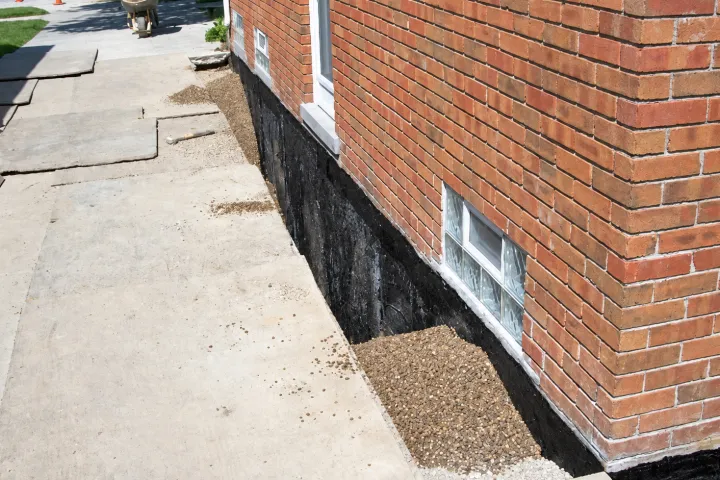 Tarred foundation wall beside an open trench along a brick home
