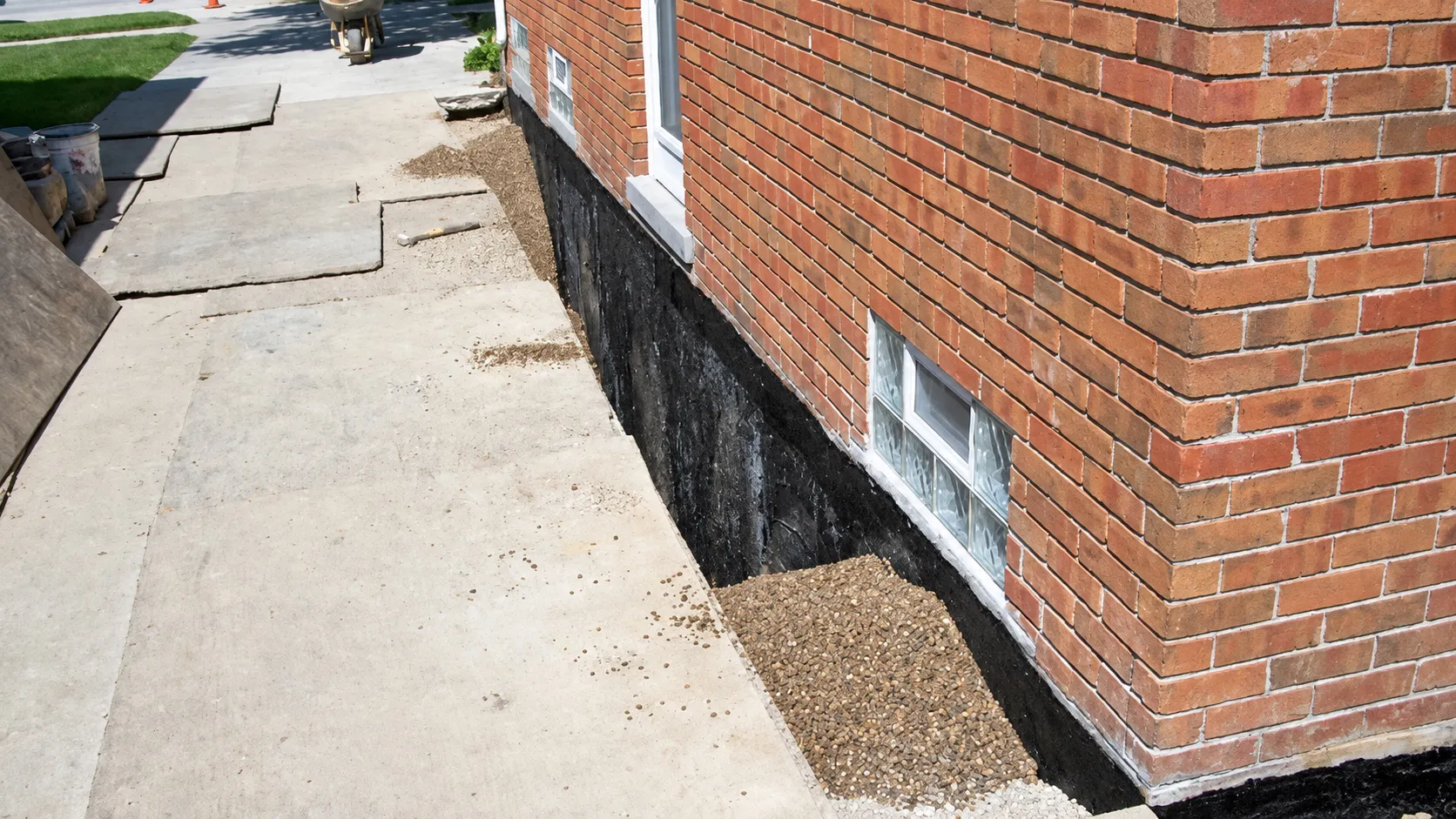 Tarred foundation wall beside an open trench along a brick home